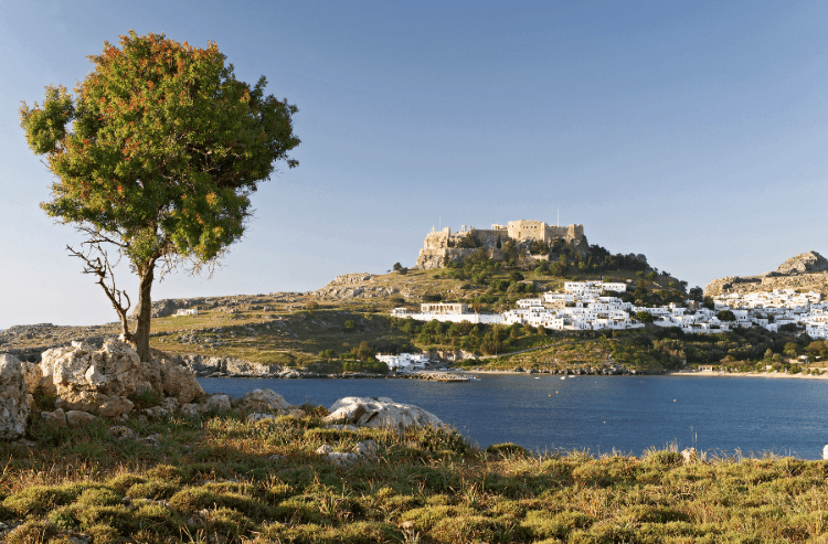 Photo of the town of Lindos and the Castle of the Knights of St John above it from across the water.