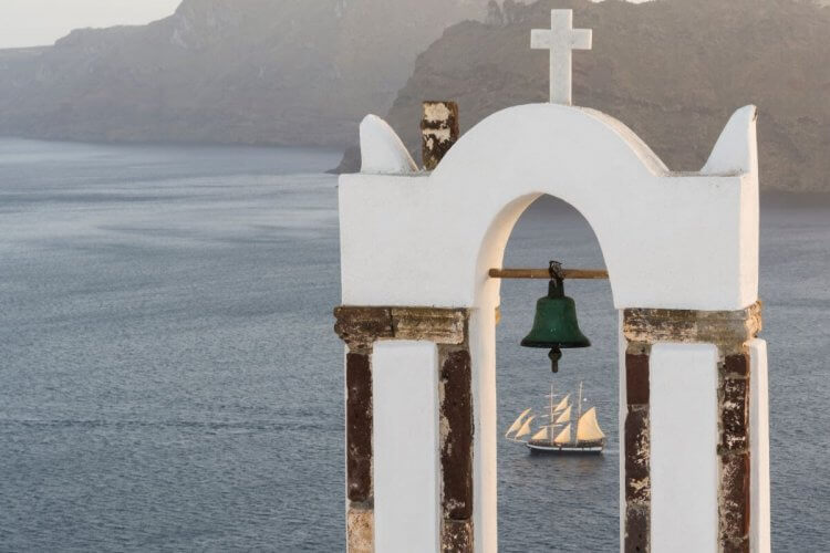 Traditional church belfry and sailing boat at sunset in Oia, Santorini, Greece